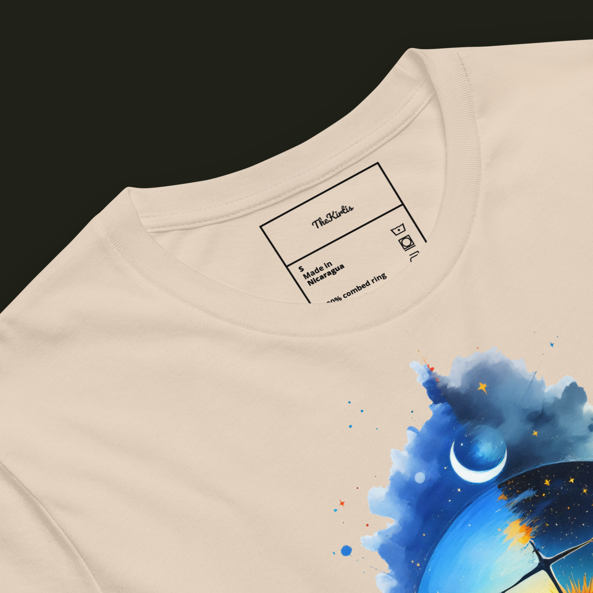 Close-up of the Cosmic Balance artwork on a soft cream unisex t-shirt showing the scale, sun, crescent moon and star-filled sky.