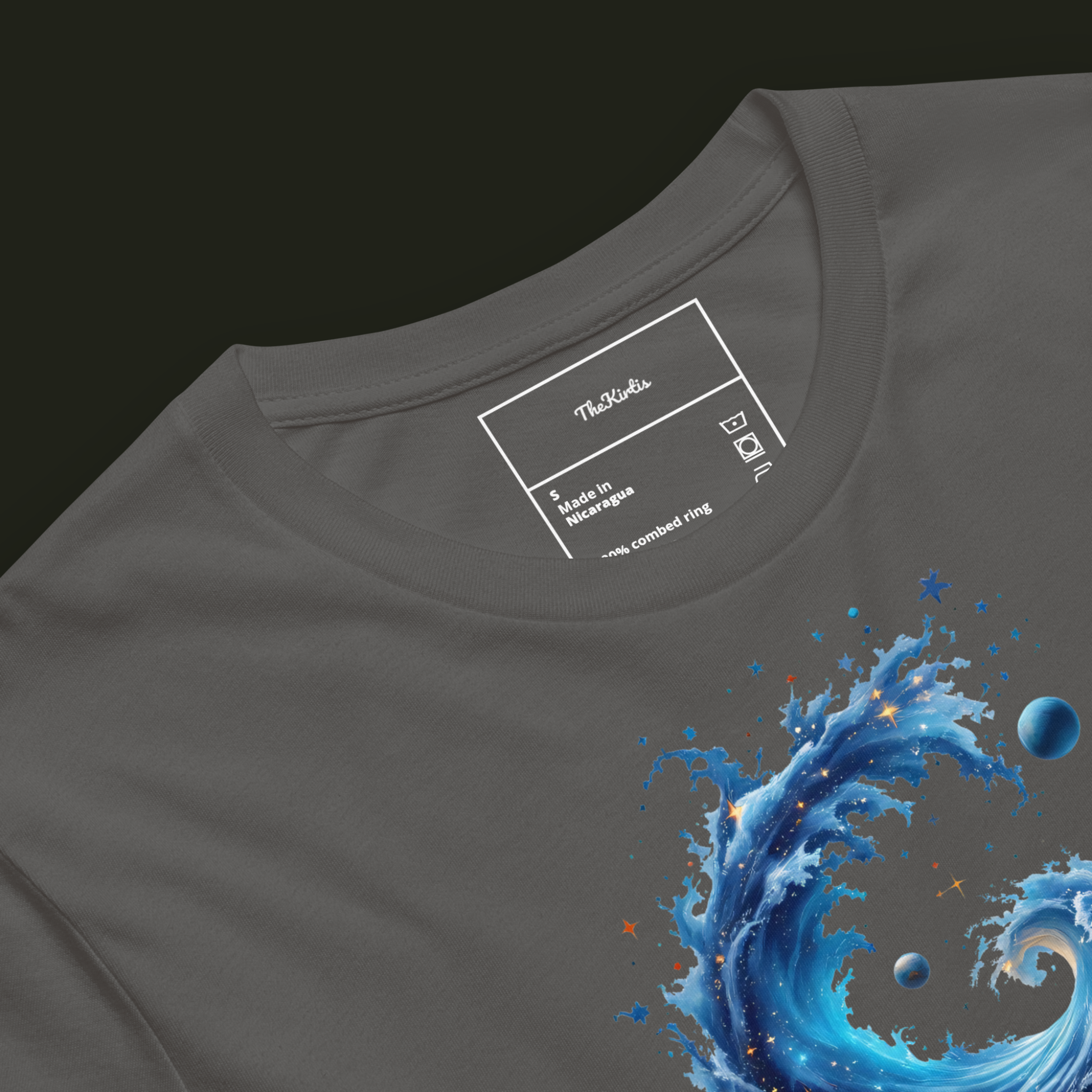 Close-up of the Cosmic Tide artwork on an asphalt unisex t-shirt showing swirling cosmic ocean waves with stars and planets.